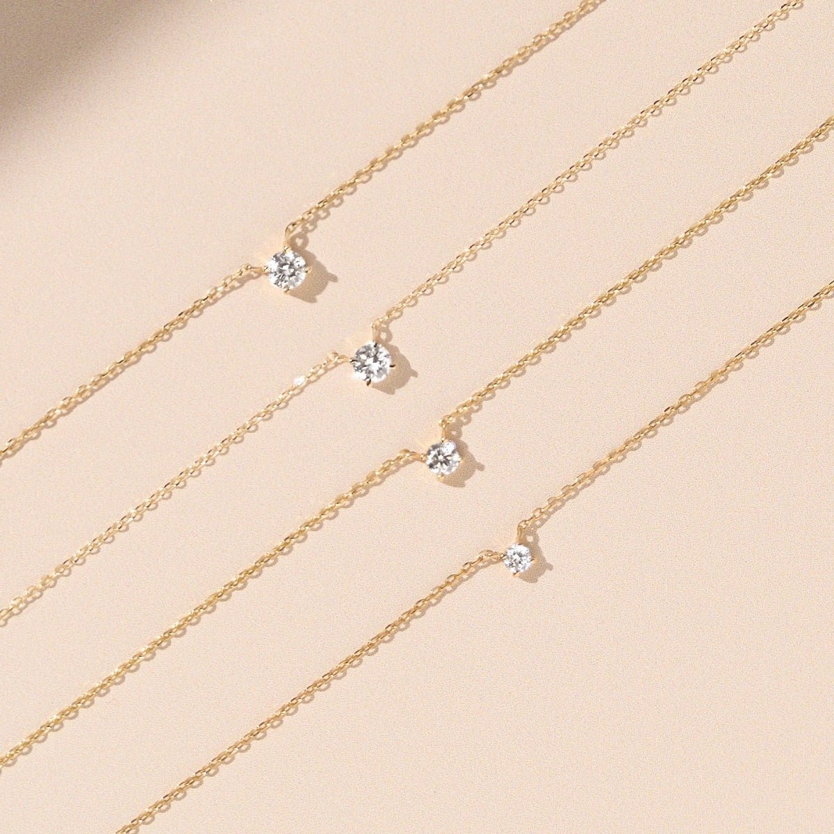 close-up of five 14k gold diamond solitaire necklaces on beige background, varying diamond sizes shown side by side