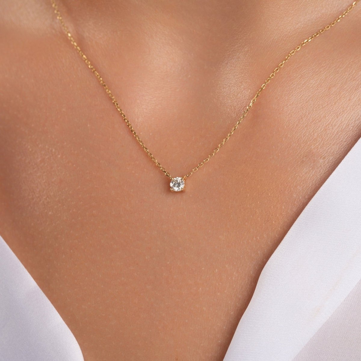14k yellow gold solitaire diamond necklace worn by a woman with a white dress, close-up on the collarbone