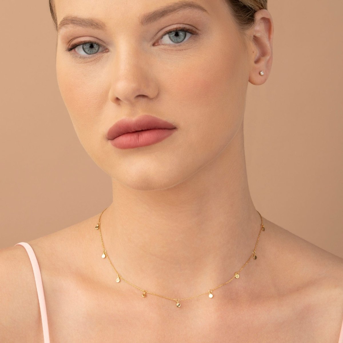 Blonde model wearing minimalist gold charm necklace with fine chain and evenly spaced discs.