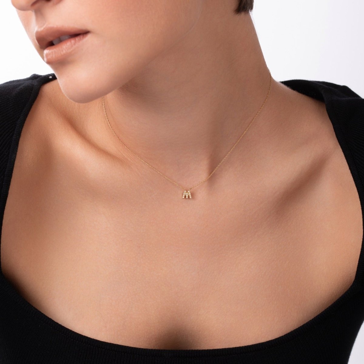 Woman wearing a gold "M" initial pendant necklace resting at the collarbone – dainty and minimal style.