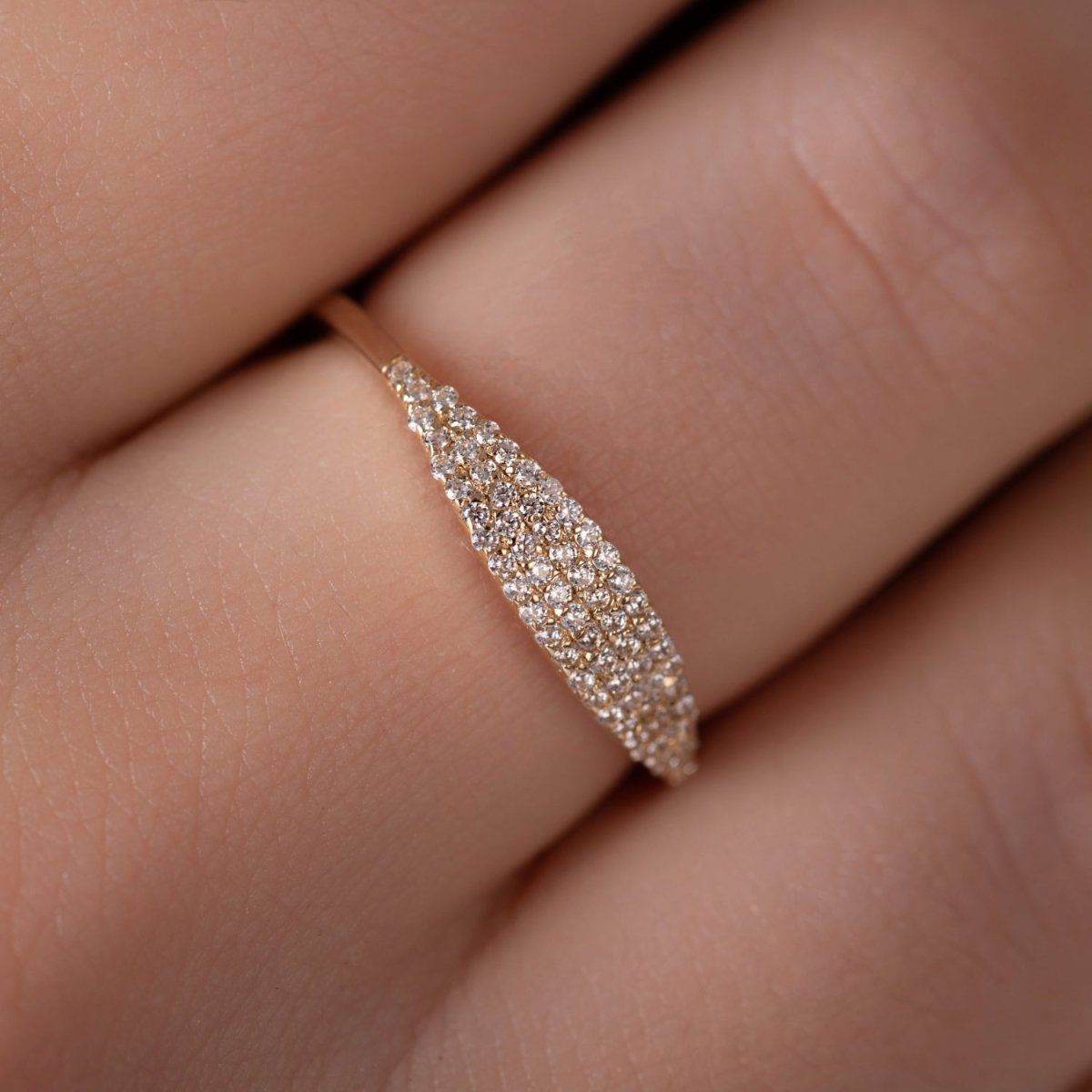 A close-up of a woman’s hand wearing a 14k yellow gold pavé diamond band, capturing the intricate rows of shimmering diamonds and the ring’s refined elegance.