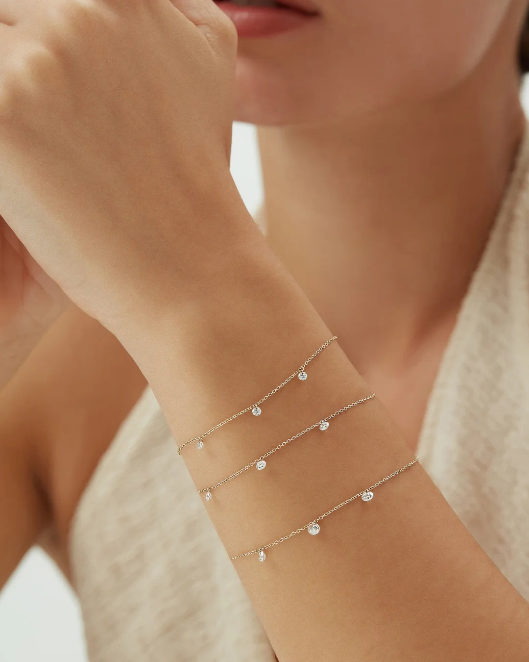 Close-up of a woman’s wrist adorned with three dainty 14k gold bracelets, each featuring evenly spaced dangling diamonds for a delicate, layered look.