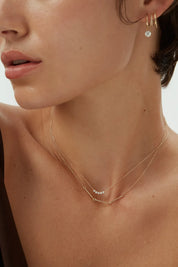 Close-up view of a woman wearing a 14k yellow gold Iris Necklace with bar and loop detail, layered with a diamond dot necklace.