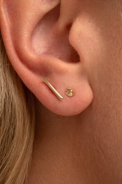 Close-up of a model wearing a single yellow gold stud earring in her helix piercing.