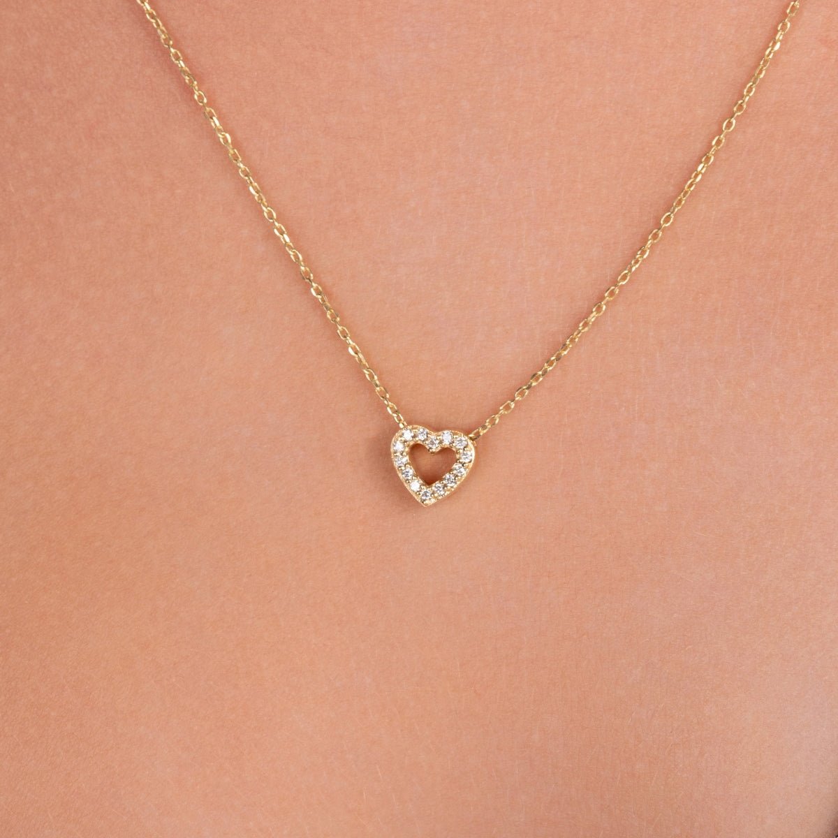 Close-up of a pavé diamond open heart necklace in yellow gold, worn on the neck, showcasing the pendant resting just below the collarbone.