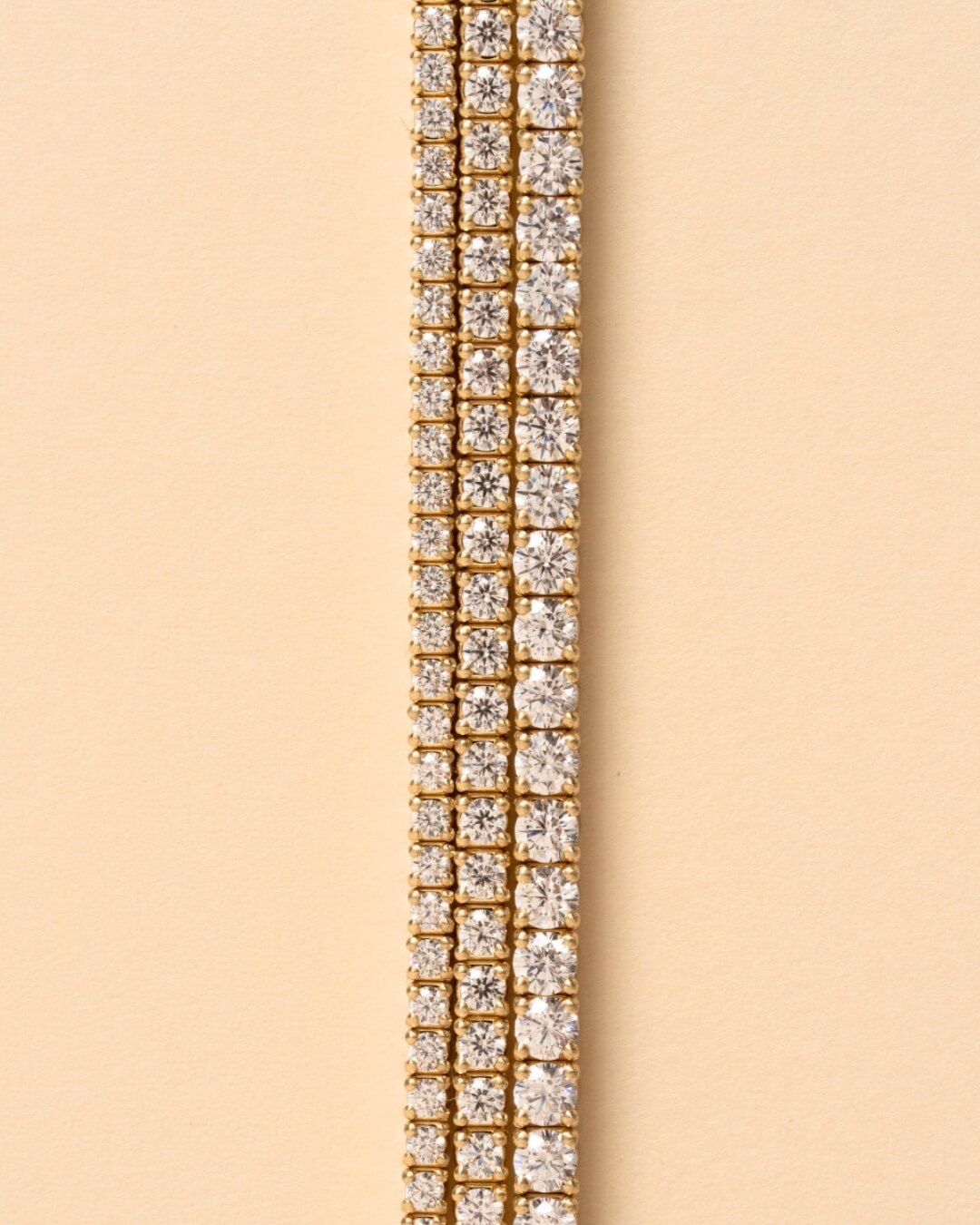 Three Diamond Tennis Bracelets placed one next to the other on a beige-colored surface