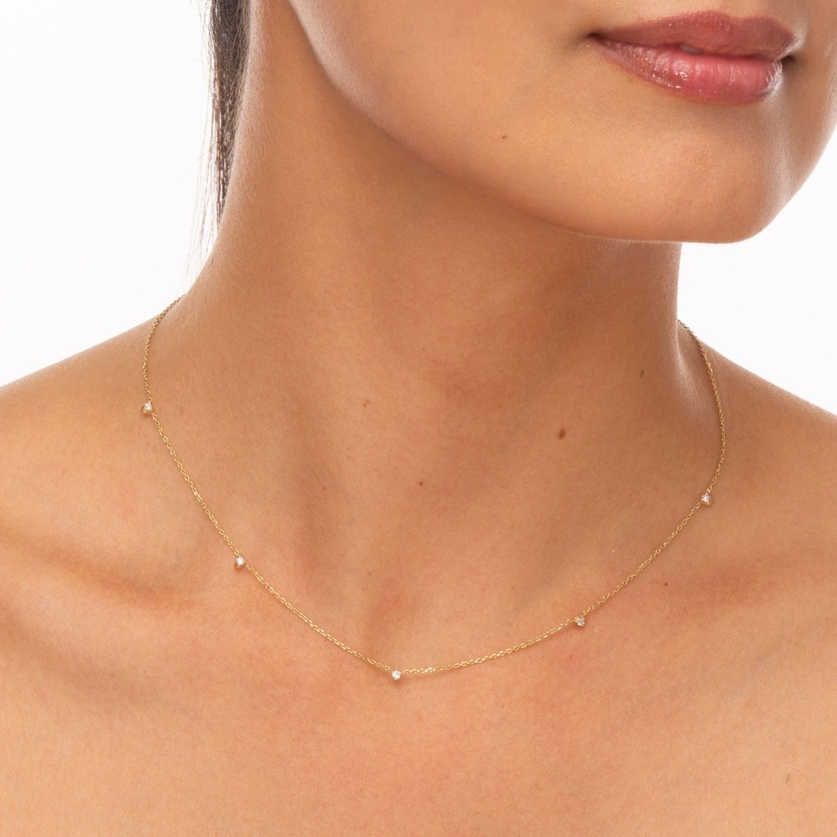 Model wearing a dainty yellow gold necklace with floating bezel-set diamonds across the collarbone.