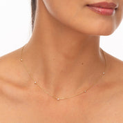 Model wearing a dainty yellow gold necklace with floating bezel-set diamonds across the collarbone.