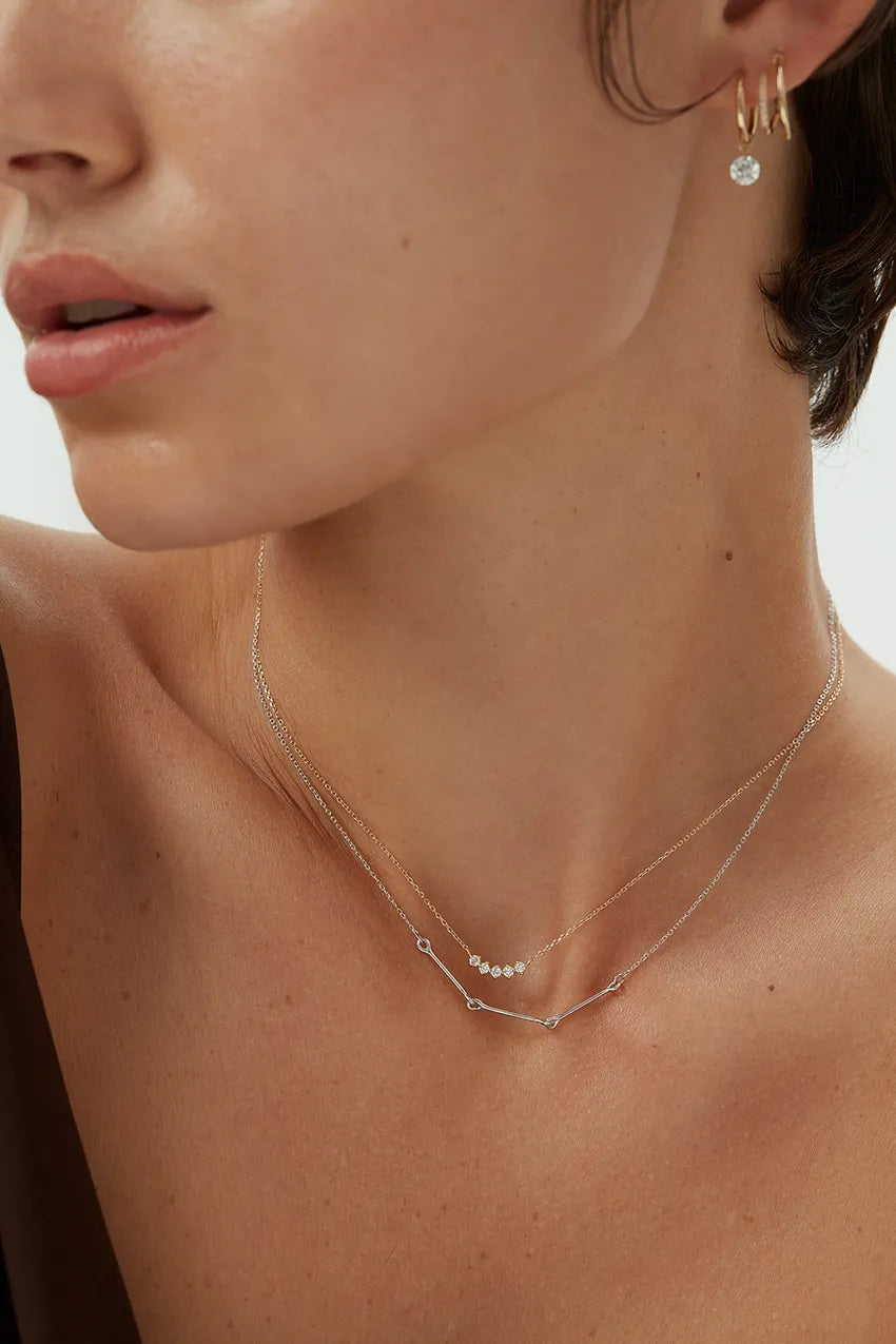 Close-up view of a woman wearing a 14k white gold Iris Necklace with bar and loop detail, layered with a diamond dot necklace.