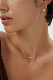 Close-up view of a woman wearing a 14k white gold Iris Necklace with bar and loop detail, layered with a diamond dot necklace.