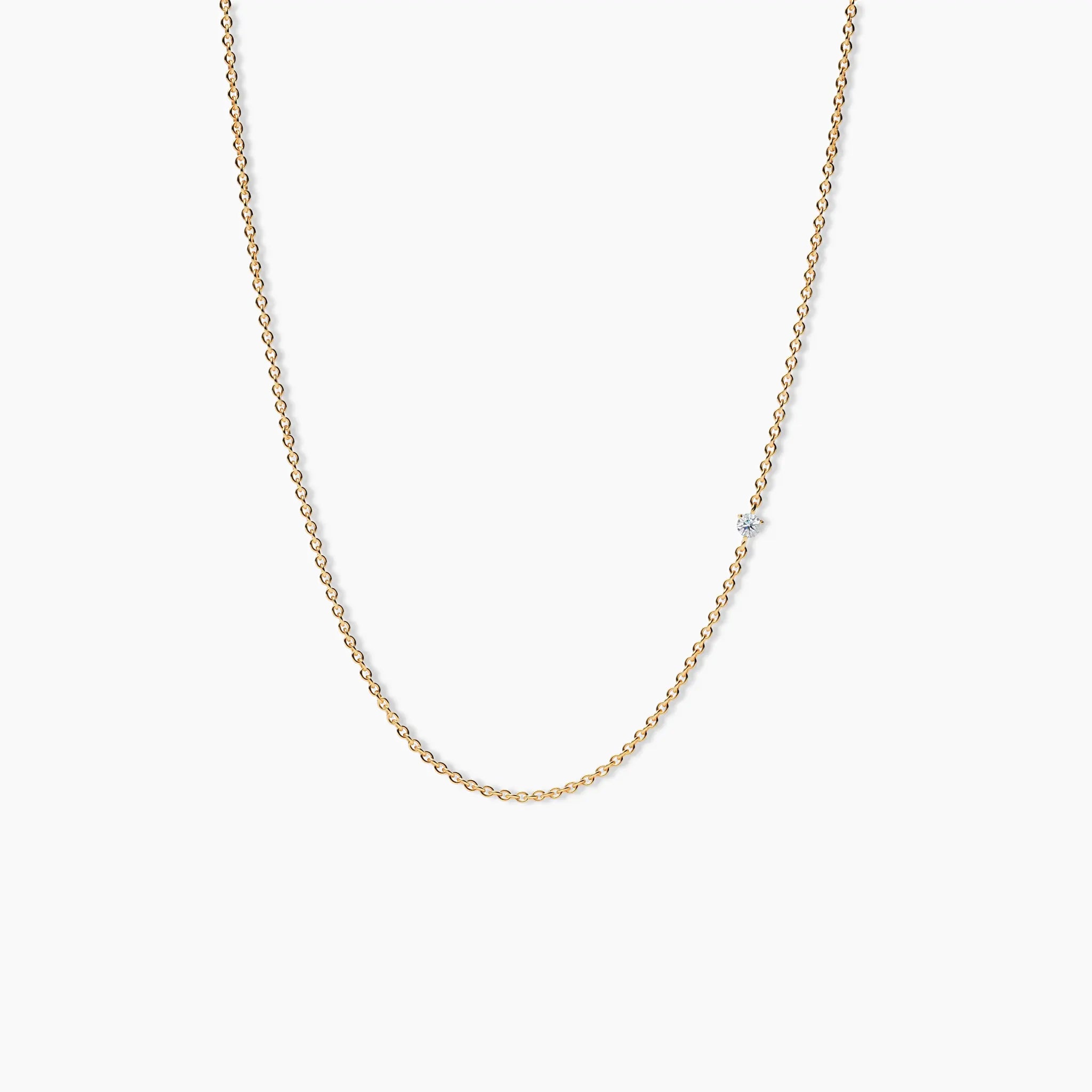 Close-up of a yellow gold necklace with a single small diamond set along a delicate chain, shown on a clean white background.