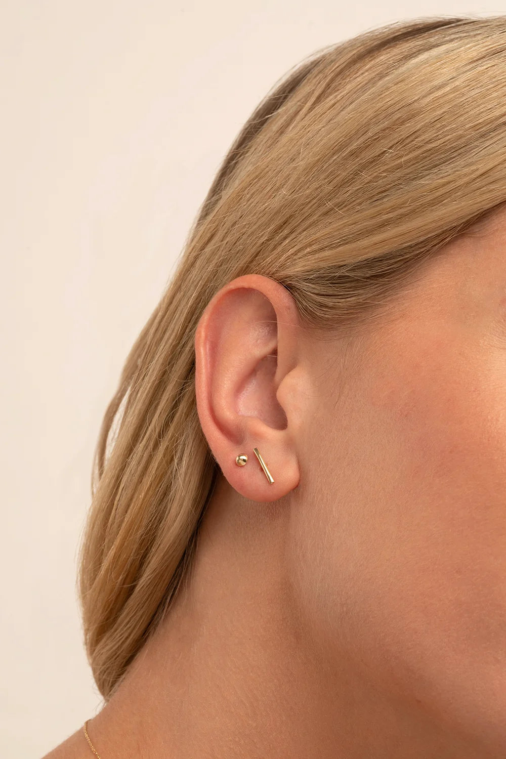 Side profile of a model with blonde hair wearing a single yellow gold point stud in her earlobe.