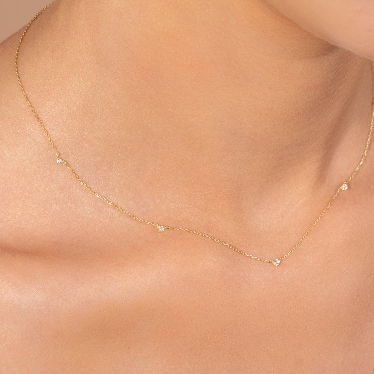 Close-up of a woman wearing a yellow gold diamond station necklace featuring five small round diamonds spaced along a fine chain.