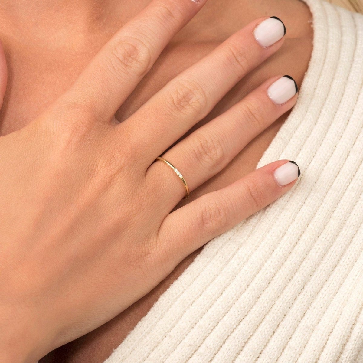 A woman’s hand styled with a 14k yellow gold slim diamond band, emphasizing its delicate and minimalist design with three subtly placed round diamonds.