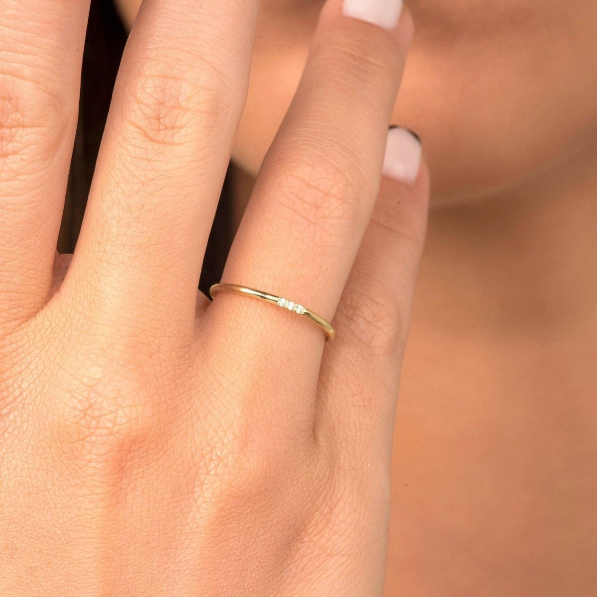 A woman wearing a 14k yellow gold slim diamond band, resting her hand on soft knit fabric. The trio of diamonds adds a subtle yet elegant touch.