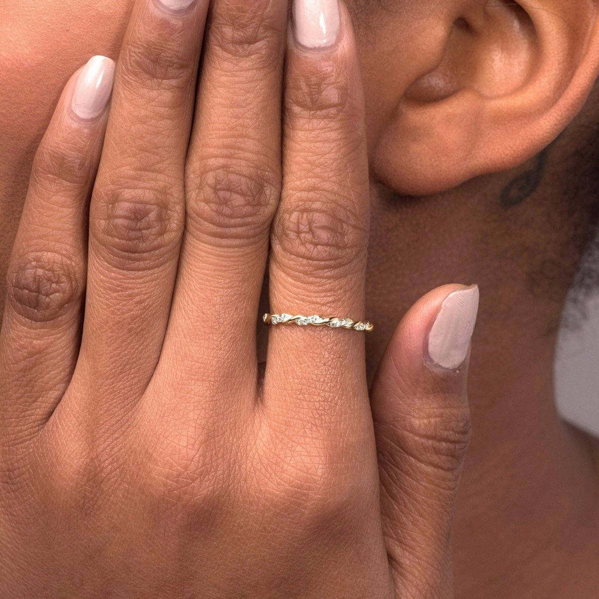 A close-up of a woman wearing a 14k rose gold twisted diamond eternity band on her index finger, highlighting its elegant twisted shape and sparkling diamonds.
