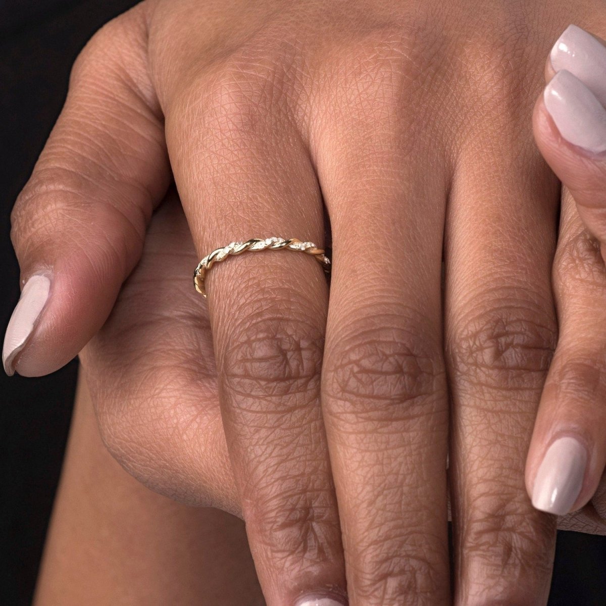 A close-up of a woman’s hand wearing a 14k yellow gold twisted diamond eternity band on her index finger, showcasing the intricate twist design and sparkling diamonds.