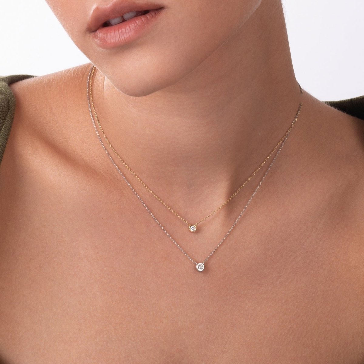 Close-up of a woman wearing two minimalist bezel-set diamond necklaces, one in 14k yellow gold and the other in white gold, layered elegantly at the collarbone.
