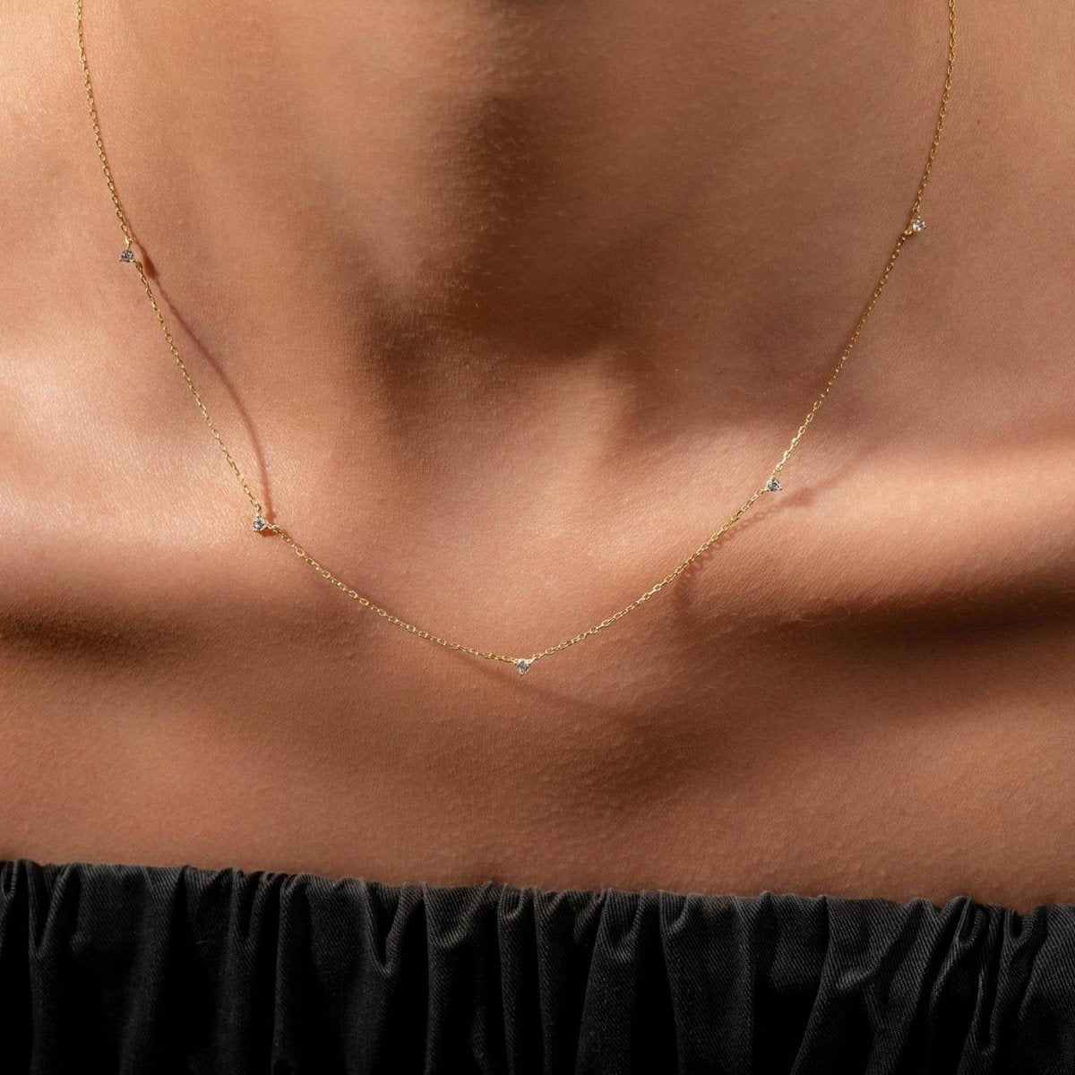 Model wearing a yellow gold diamond station necklace with five tiny round diamonds delicately spaced along the collarbone.