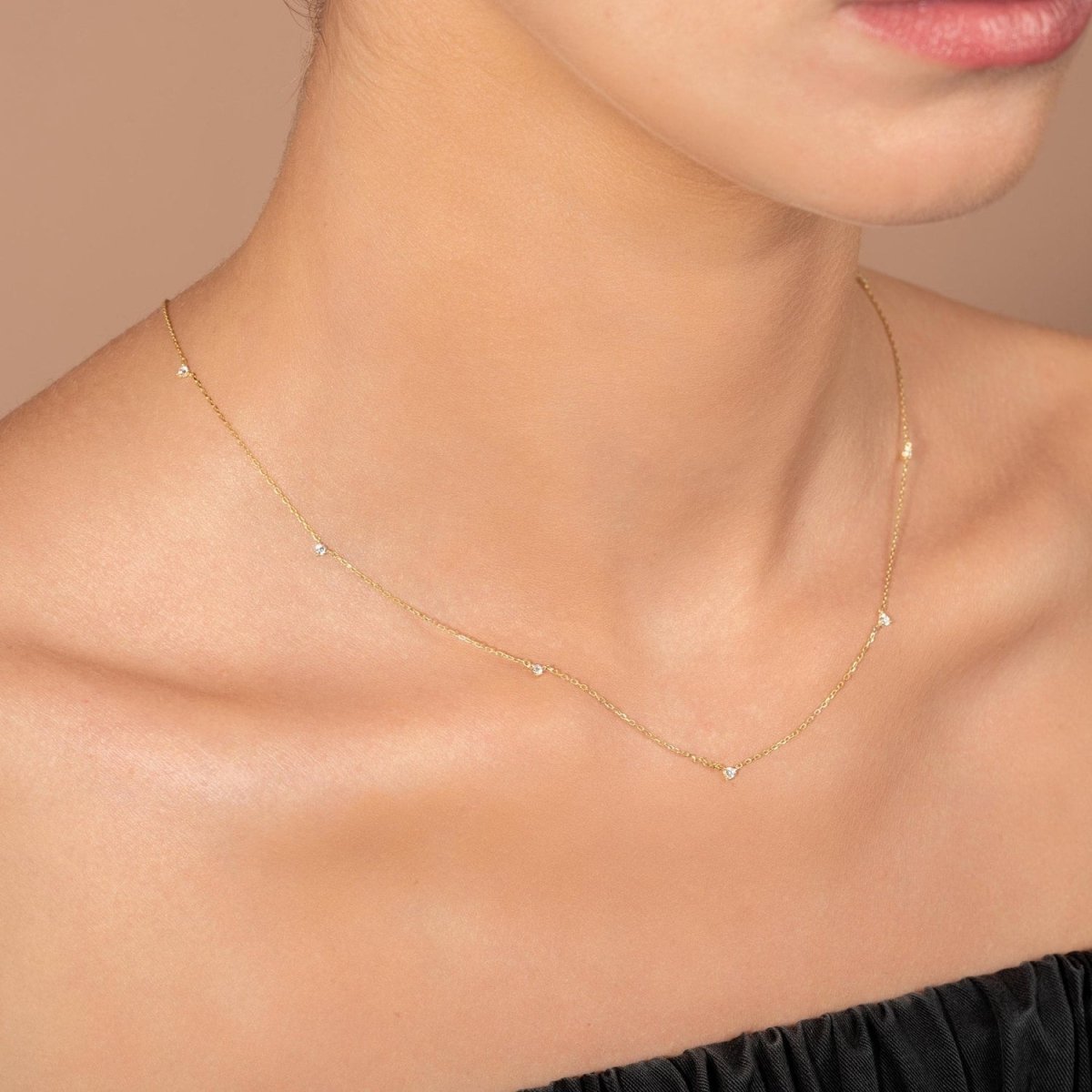 Model wearing a fine yellow gold necklace with small white diamonds spaced along the chain, styled against bare skin and a black strapless top.