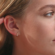 A video of a woman wearing 14k yellow gold diamond huggie hoop earrings, moving naturally to showcase the snug fit and subtle sparkle of the round brilliant-cut diamond.