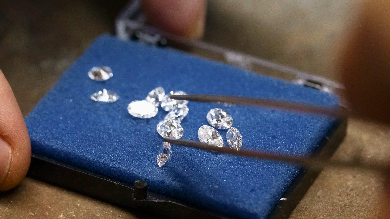 Loose lab grown diamonds in various cuts displayed on blue gemstone pad, selected by hand with tweezers in the Enea Studio Athens workshop