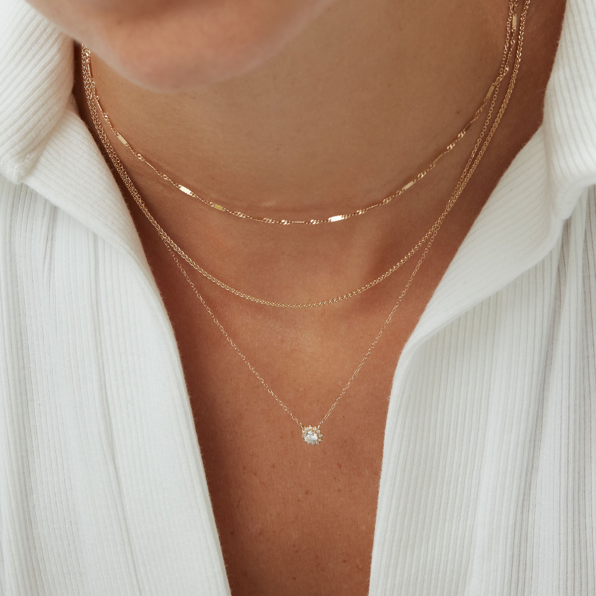 Layered solid 14k gold necklaces in varying lengths on neutral background by ENEA Studio