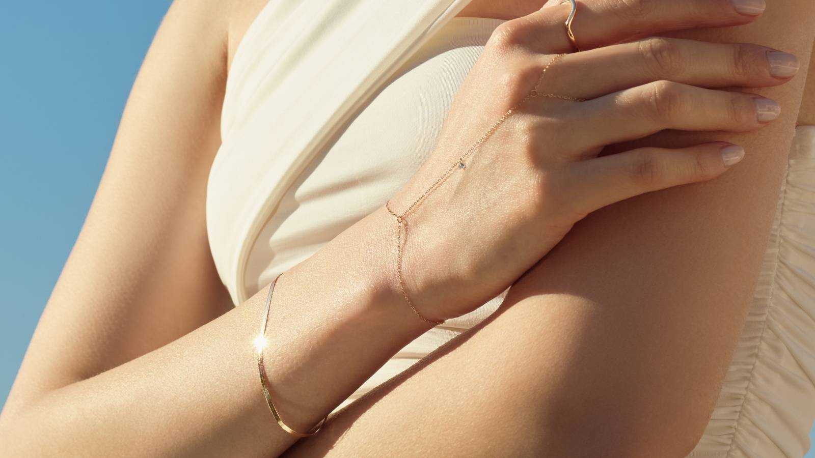 Close photo of a woman's hand wearing a plain 14k gold chain bracelet and a hand chain with a tiny diamond - ENEA