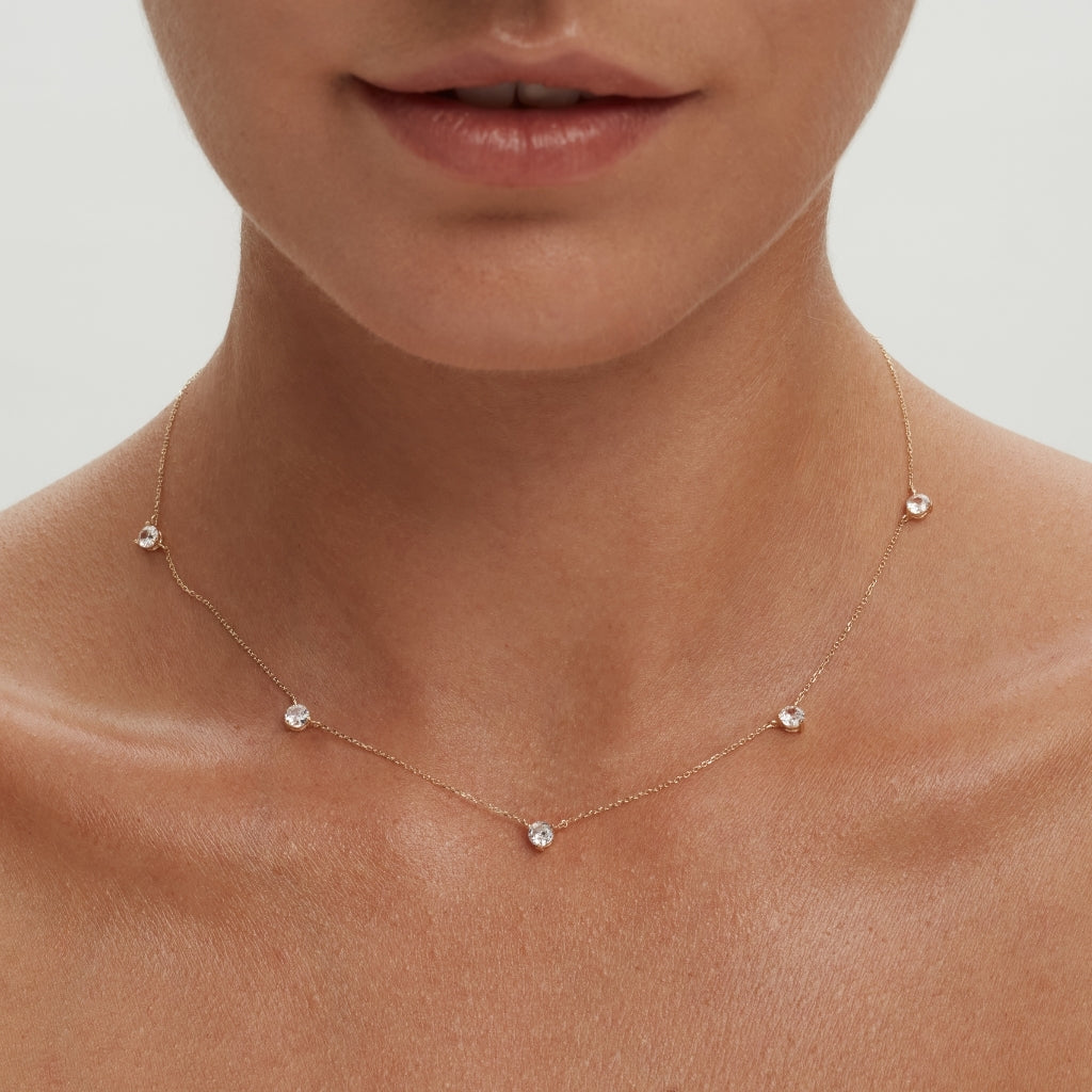 Portait of a woman in a beige background wearing a 14k gold station necklace set with five white diamonds equally spaced on the chain-ENEA
