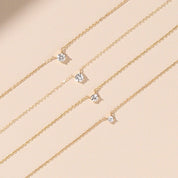 close-up of five 14k gold diamond solitaire necklaces on beige background, varying diamond sizes shown side by side
