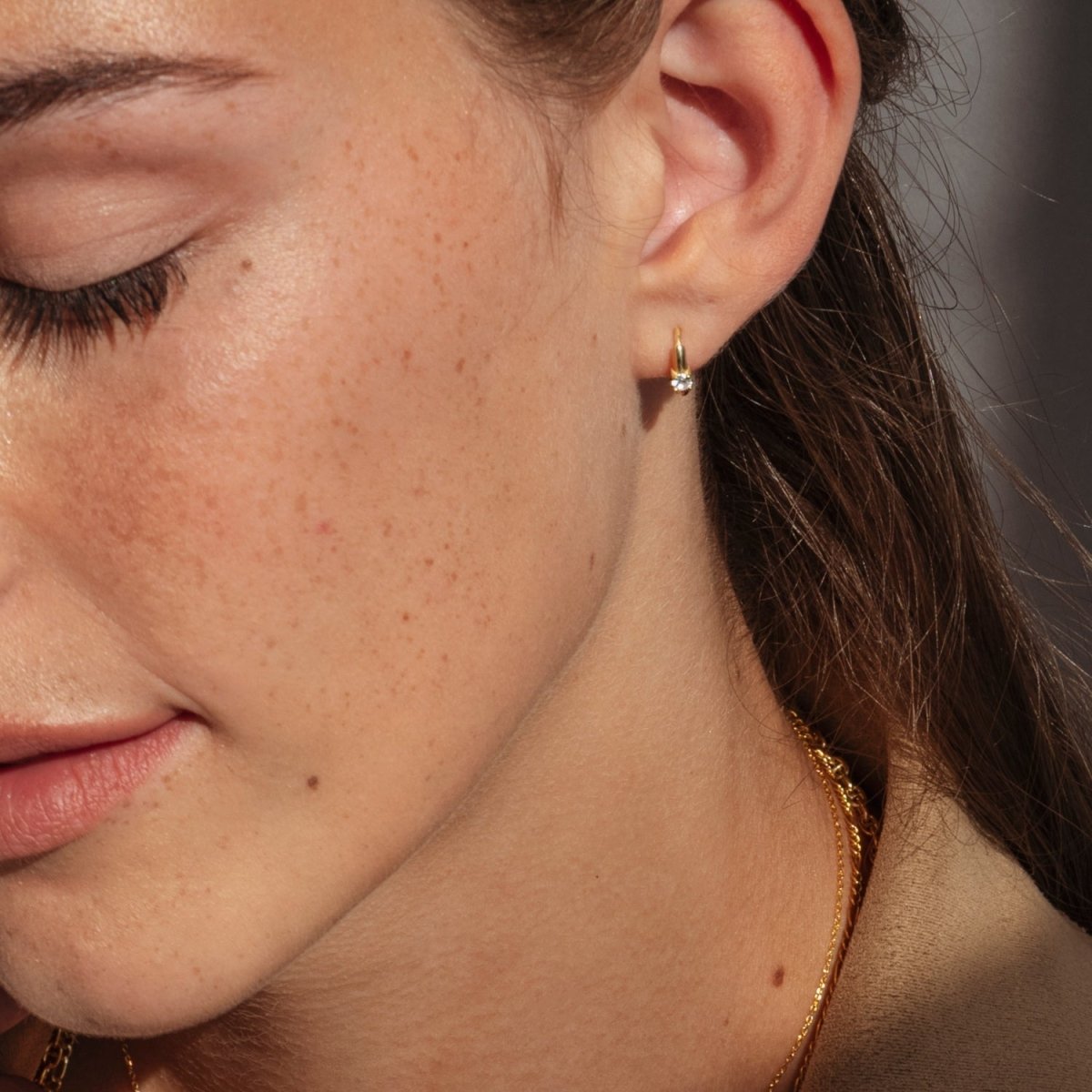 A close-up of a woman wearing a 14k yellow gold diamond huggie hoop earring, highlighting its sleek, minimal design and sparkling round diamond.
