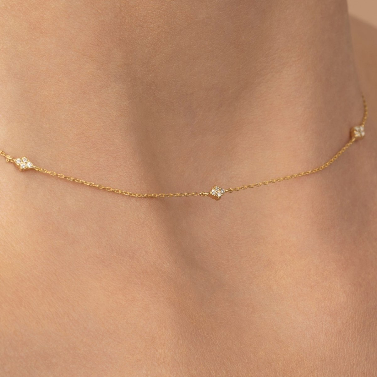 Detailed view of the station necklace resting on the neckline, showcasing 14k yellow gold and round diamonds.
