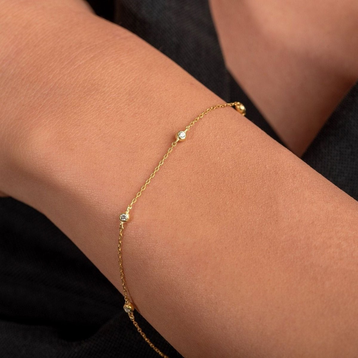 Model wears a 14k gold station bracelet with bezel-set diamonds, catching light naturally across the wrist.

