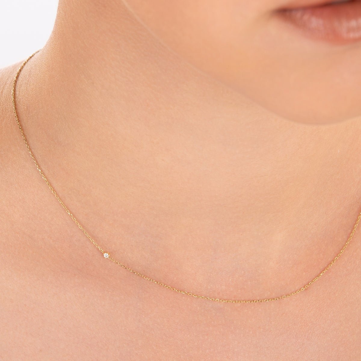 Model wearing the diamond choker necklace in yellow gold; the diamond sits side on the neck, styled with bare skin under soft lighting.

