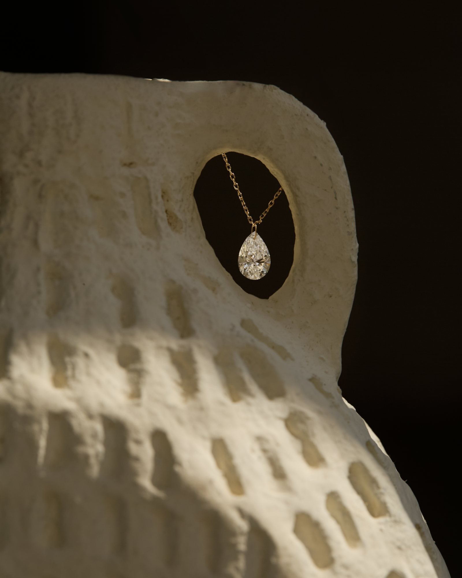 Pear-cut diamond pendant on a fine gold chain, hanging in the opening of a carved ceramic vessel