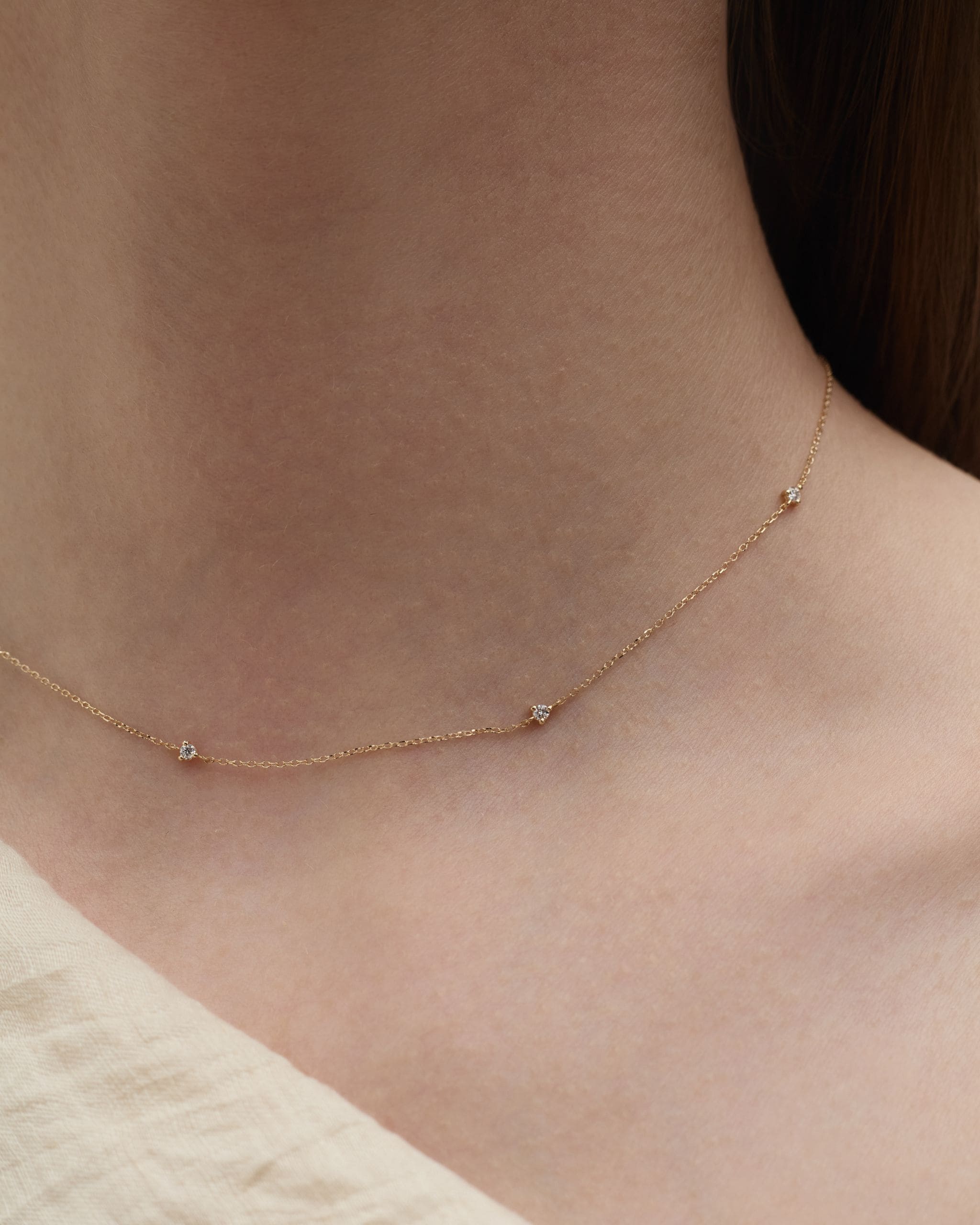 Close up on a woman's neck wearing a solid gold tiny diamond necklace featuring five small diamonds along a delicate gold chain. Enea Studio