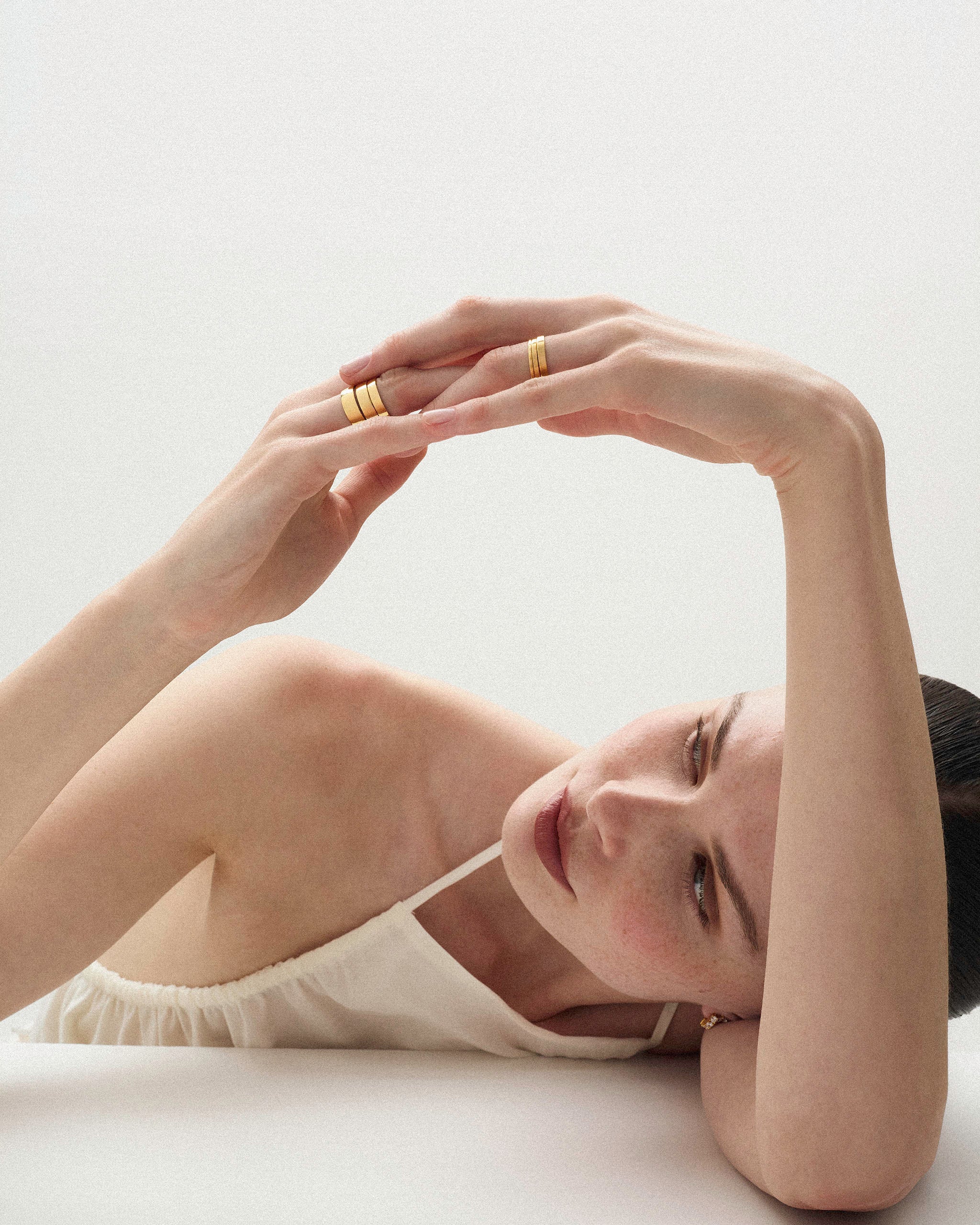 Woman lying her arm and head on a white surface wearing the Cigar Band Ring in yellow gold and in 6 different widths on her fingers