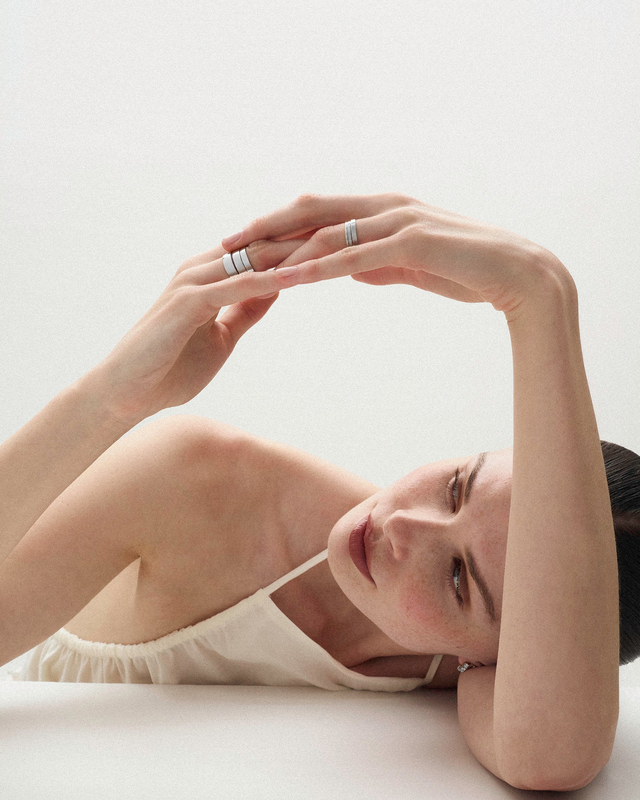 Woman lying her arm and head on a white surface wearing the Cigar Band Ring in white gold and in 6 different widths on her fingers