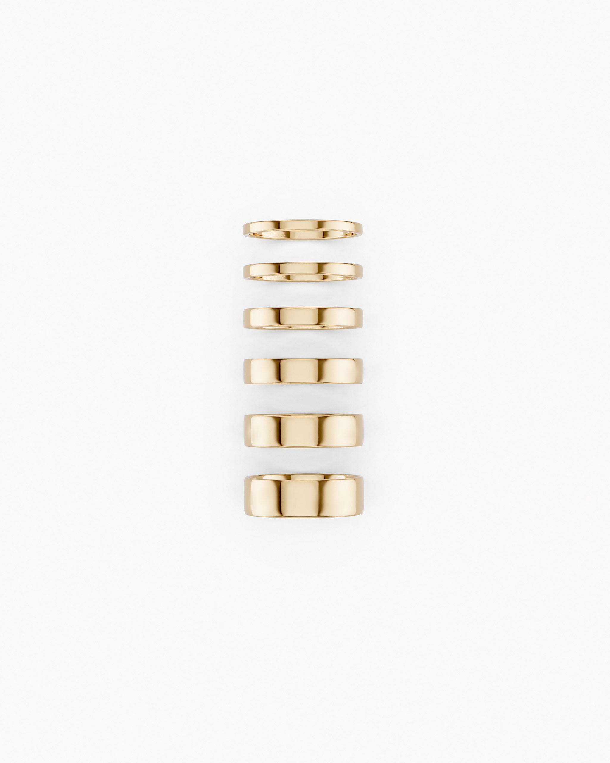 Six Cigar Band Rings made in yellow gold and in different widths stacked vertically on a white background