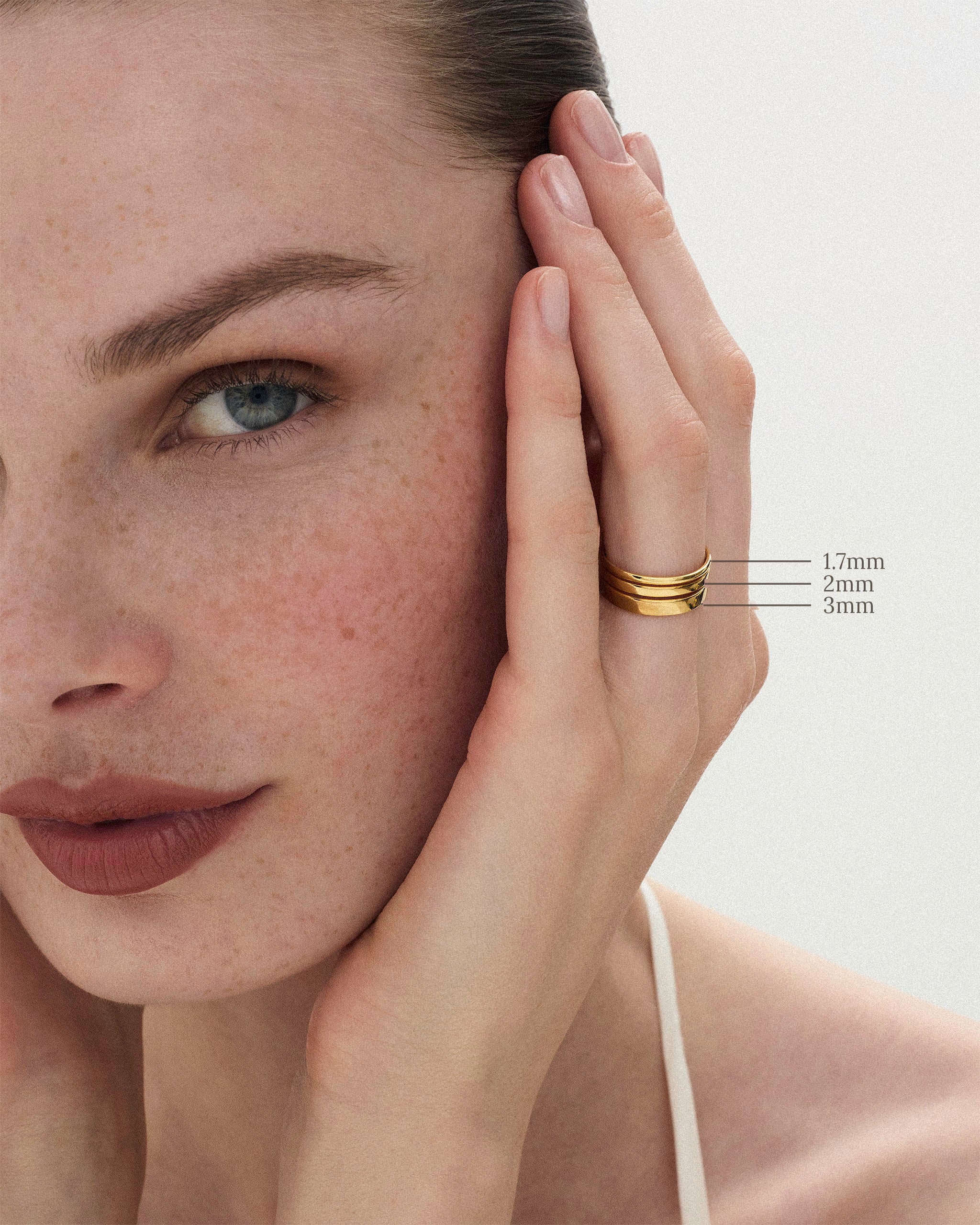 The Cigar Band Ring in 1.7mm, 2mm and 3mm widths worn stacked on a woman's finger against a neutral background 