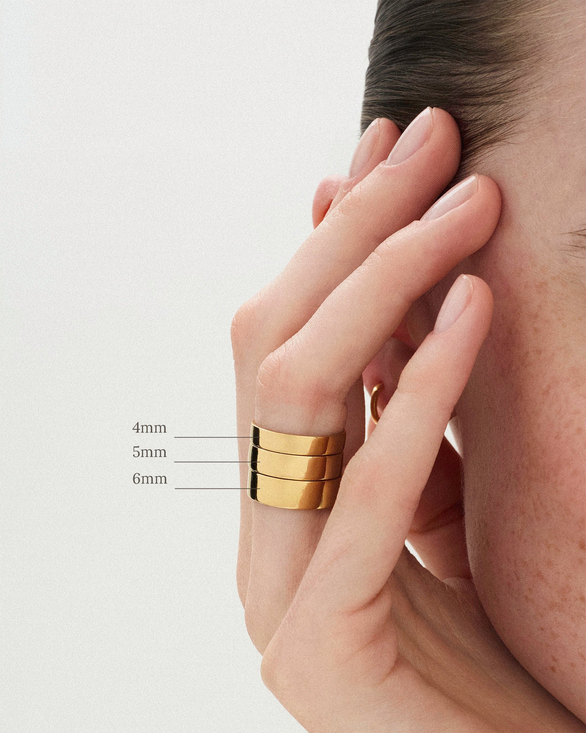 The Cigar Band Ring in 4mm, 5mm and 6mm widths worn on a woman's finger against a neutral background 