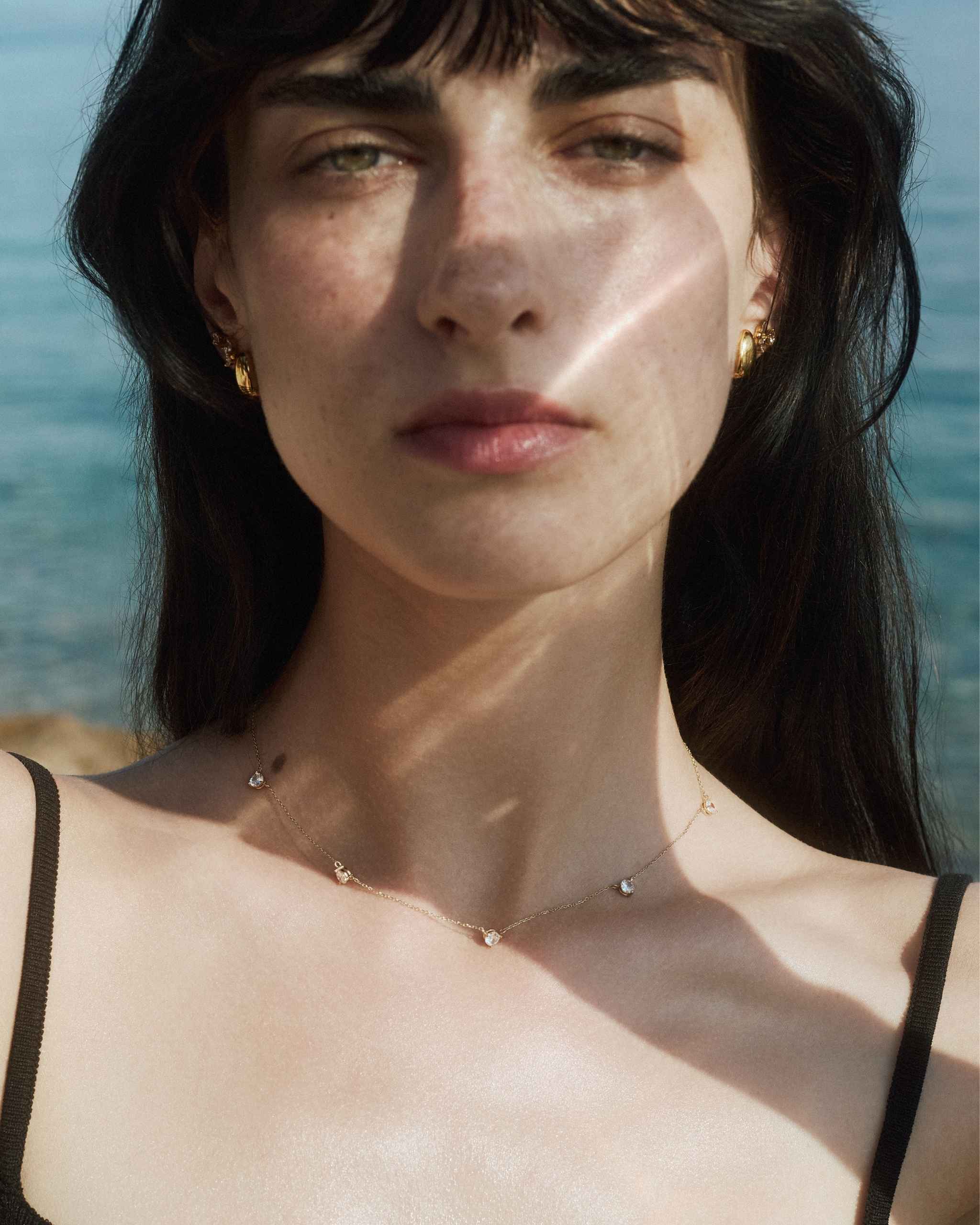 front view of the 14k yellow gold alinéa gold diamond station necklace ii worn on model on sea background