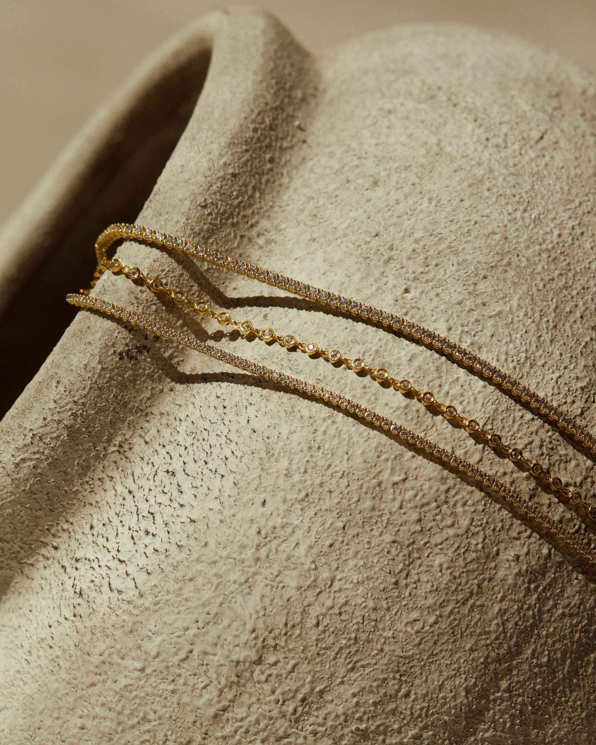 two 14k gold diamond tennis bracelets and a yellow gold diamond station bracelet laid on a textured object under soft light
