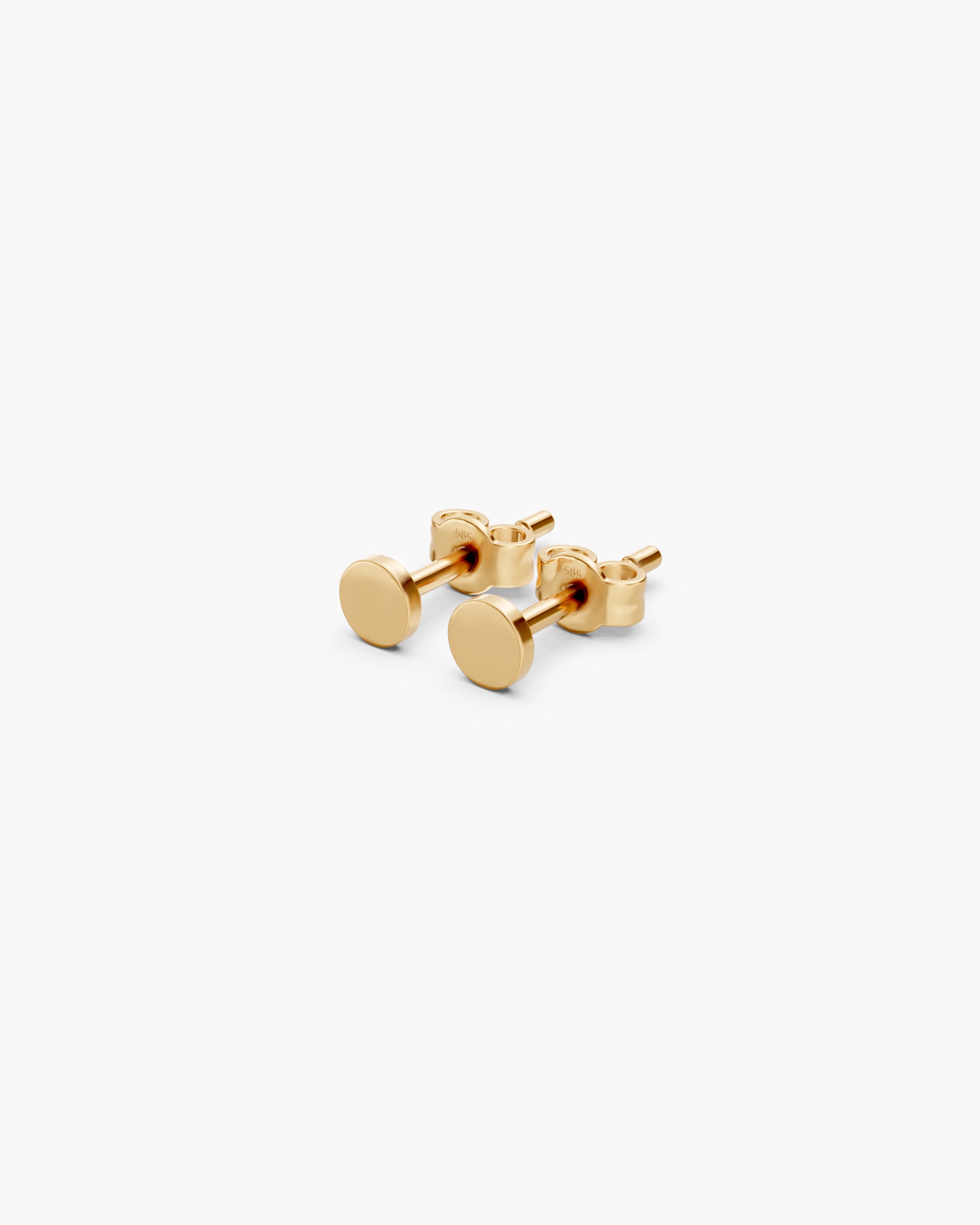 Angled view of the Diskos Disc Studs in 14k yellow gold with push back closures stamped 585, on an off-white surface. ENEA Studio