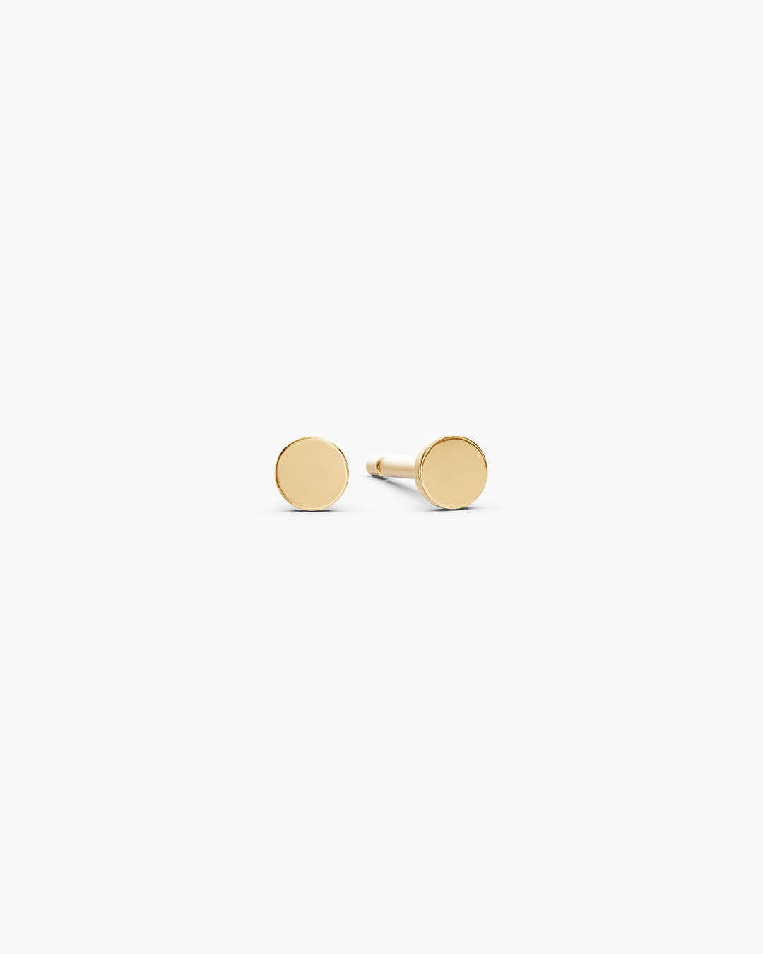 Diskos Disc Studs in 14k yellow gold, front view, a pair of 3.5mm polished flat gold disc stud earrings on an off-white surface. ENEA Studio