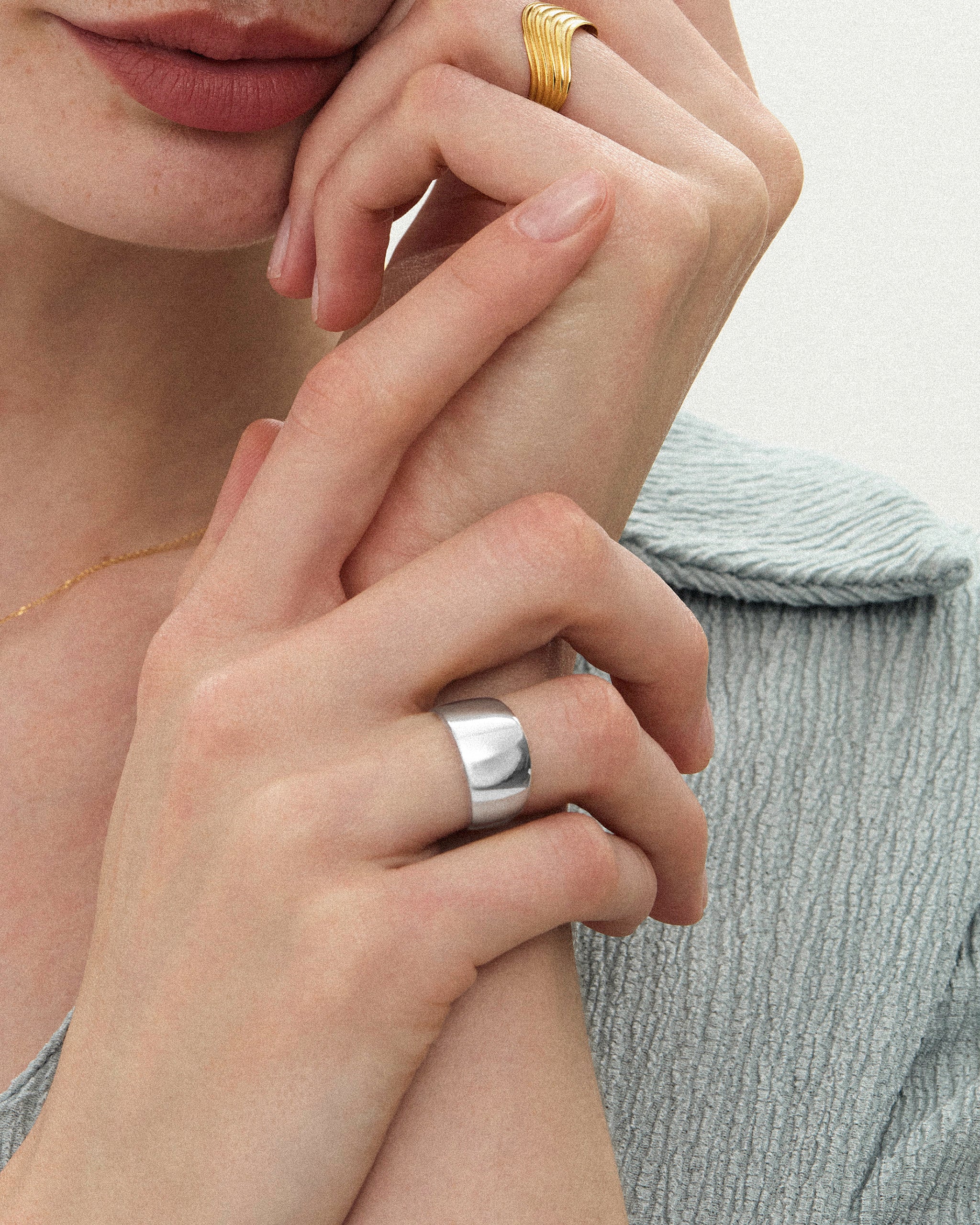 Close-up of a woman's hands styled with a yellow gold wavy ribbed band and a wide, polished band in silver on a neutral background