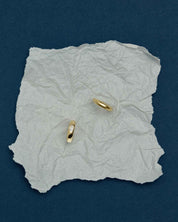 two solid gold dome rings, one plain and one set with a round diamond at its center, placed on a crumpled piece of paper on a blue surface