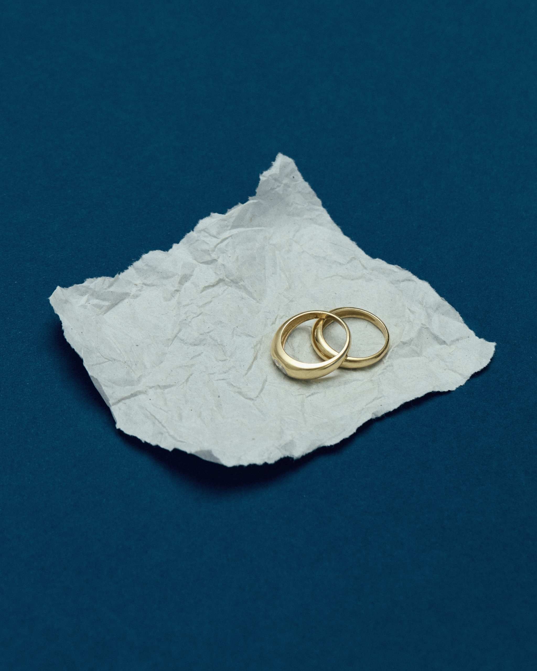 two solid gold dome rings placed on a crumpled piece of paper on a blue surface