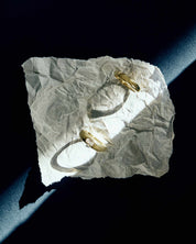 two solid gold dome rings placed on a crumpled piece of paper under strong natural light on a dark blue surface