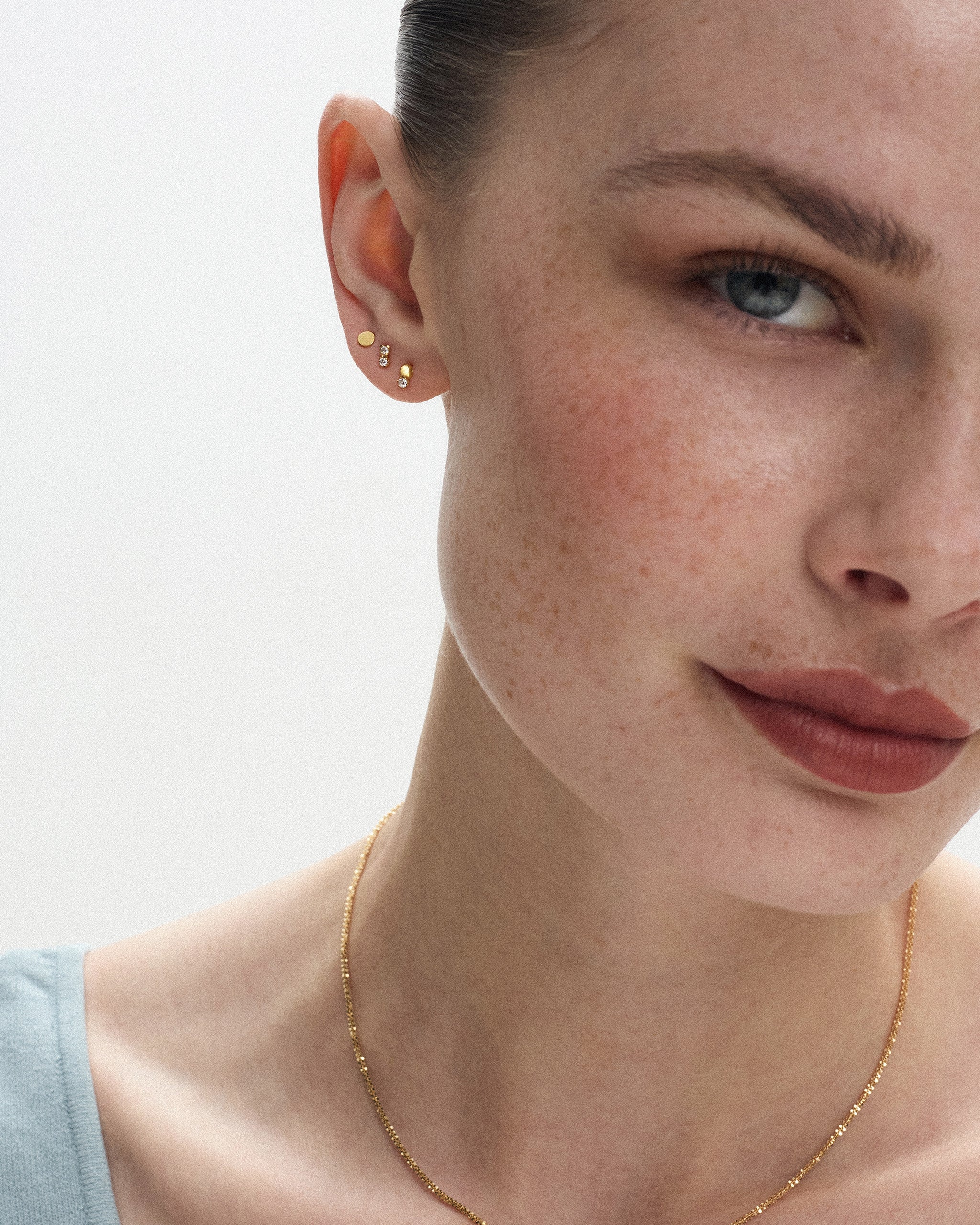 Woman wearing Dyo Diamond Bead Studs in 14k yellow gold with a fine gold chain necklace, showing the tiny diamond and gold bead earring at true scale. ENEA Studio